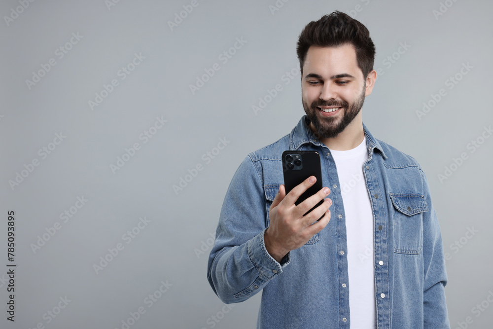 Happy young man using smartphone on grey background, space for text Happy young man using smartphone on grey background, space for text