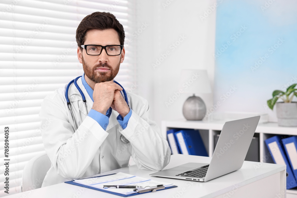 Medical consultant with glasses and stethoscope at table in clinic Medical consultant with glasses and stethoscope at table in clinic