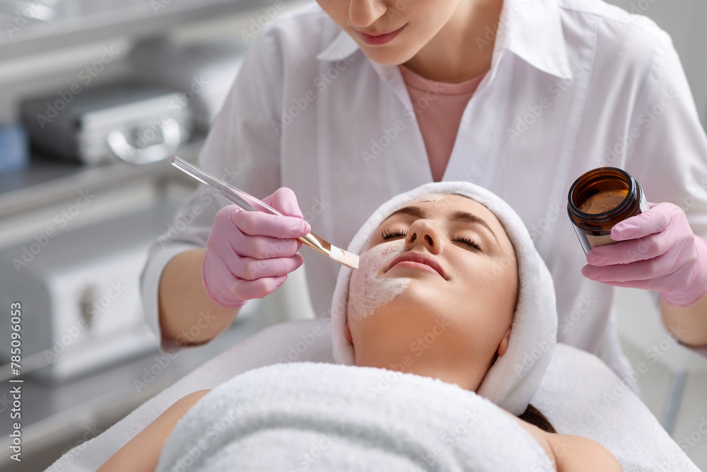 Cosmetologist applying mask on woman's face in clinic, closeup Cosmetologist applying mask on woman's face in clinic, closeup