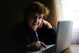 An aged woman engages with technology, her fingers tapping on a laptop keyboard. She bridges the gap between tradition and modernity, embracing the digital realm with wisdom.