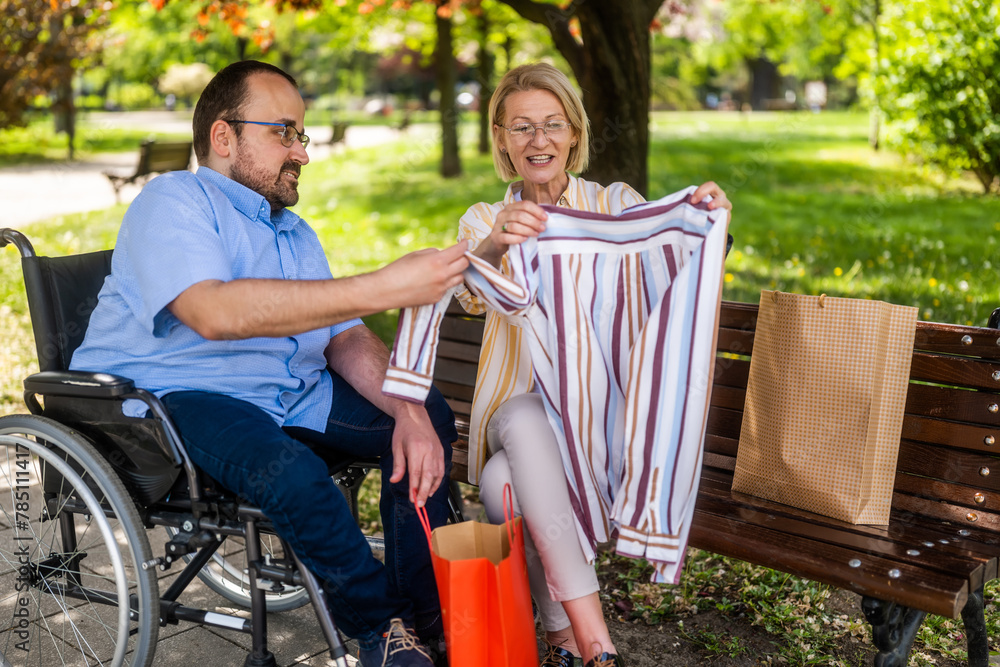 Man in wheelchair is spending time with his mother in park. They are talking after shopping. Man in wheelchair is spending time with his mother in park. They are talking after shopping.