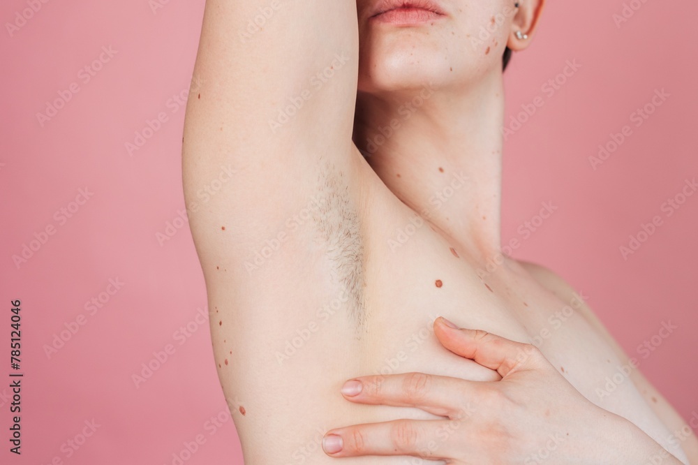 A young beautiful shirtless woman showing off her hairy armpits on an isolated pink background.