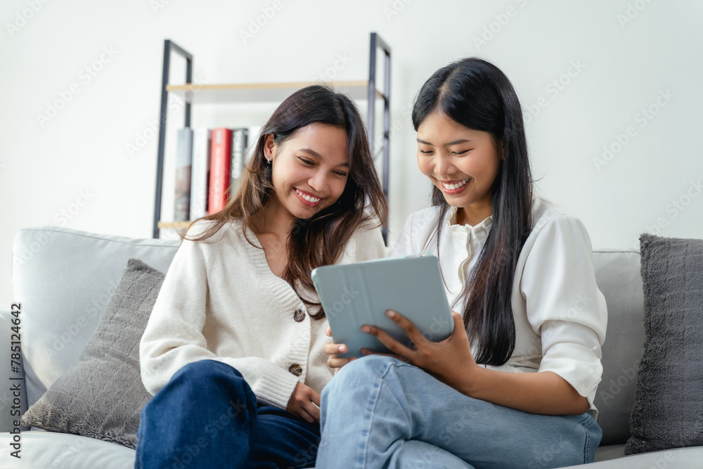 Two women sitting on a couch, one of them holding a tablet Two women sitting on a couch, one of them holding a tablet