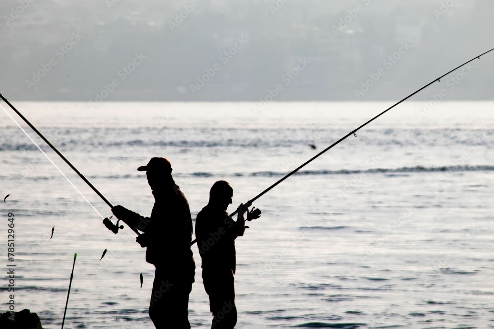 Beautiful shot of silhouette of amateur fishermen on the seashore on sea waves background Beautiful shot of silhouette of amateur fishermen on the seashore on sea waves background