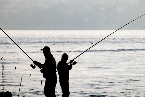 Beautiful shot of silhouette of amateur fishermen on the seashore on sea waves background