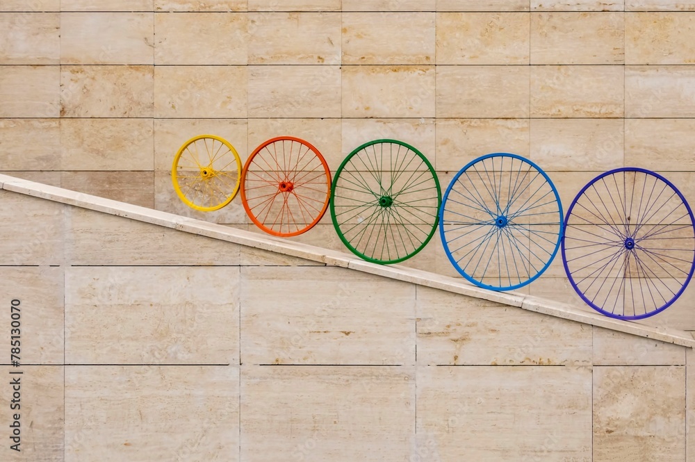 Beautiful shot of decorative rainbow colored bicycle wheels next to the beige wall