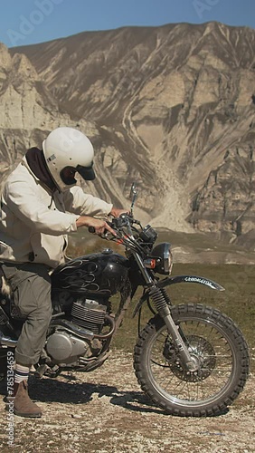 vertical ProRes shot captures a motorcyclist in a moment of anticipation as they kickstart their motorcycle before a fast departure. Dressed for adventure, the rider is set against a dramatic photo