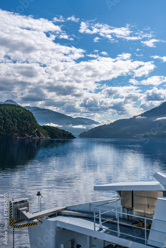 Serene stangvikfjord view from a ferry deck in Møre og Romsdal, norway on a summer sunny day. A ferry cruises through the calm waters of the fjord, with mountains and white clouds.  photo