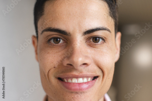 A young biracial man with short hair is smiling in a modern business office