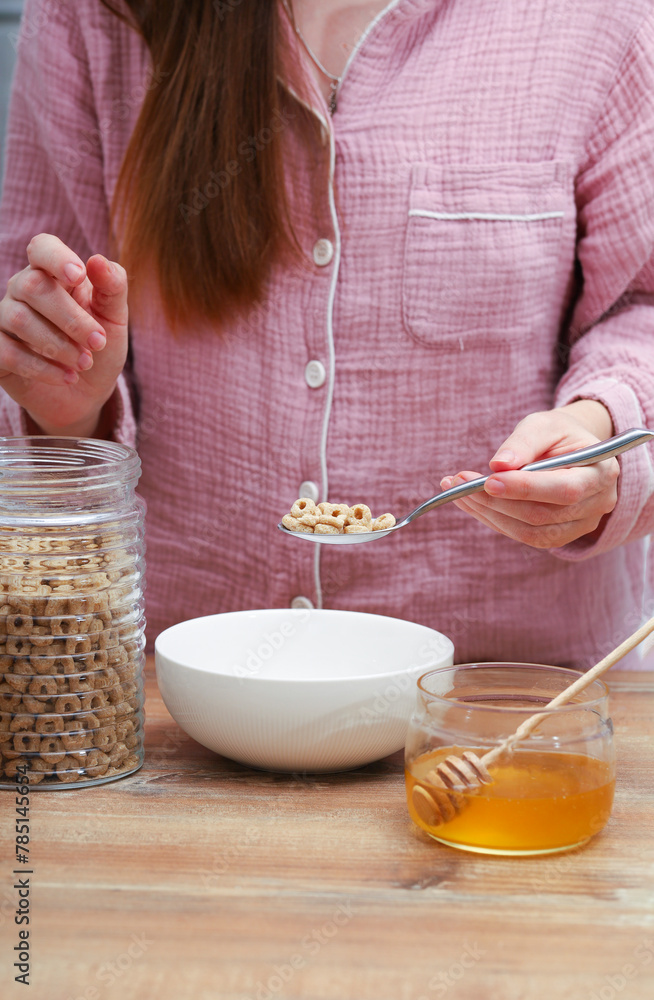 Woman female hands prepare a quick breakfast of dry round corn flakes balls, honey, milk on a kitchen.