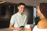 Biracial man holding smartphone talks to biracial woman in a modern business office