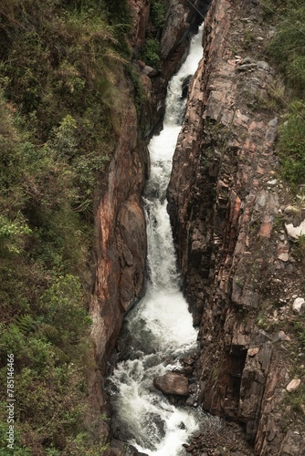 Vertical shot of a waterfall flowing through narrow rocks near Banos, Ecuador