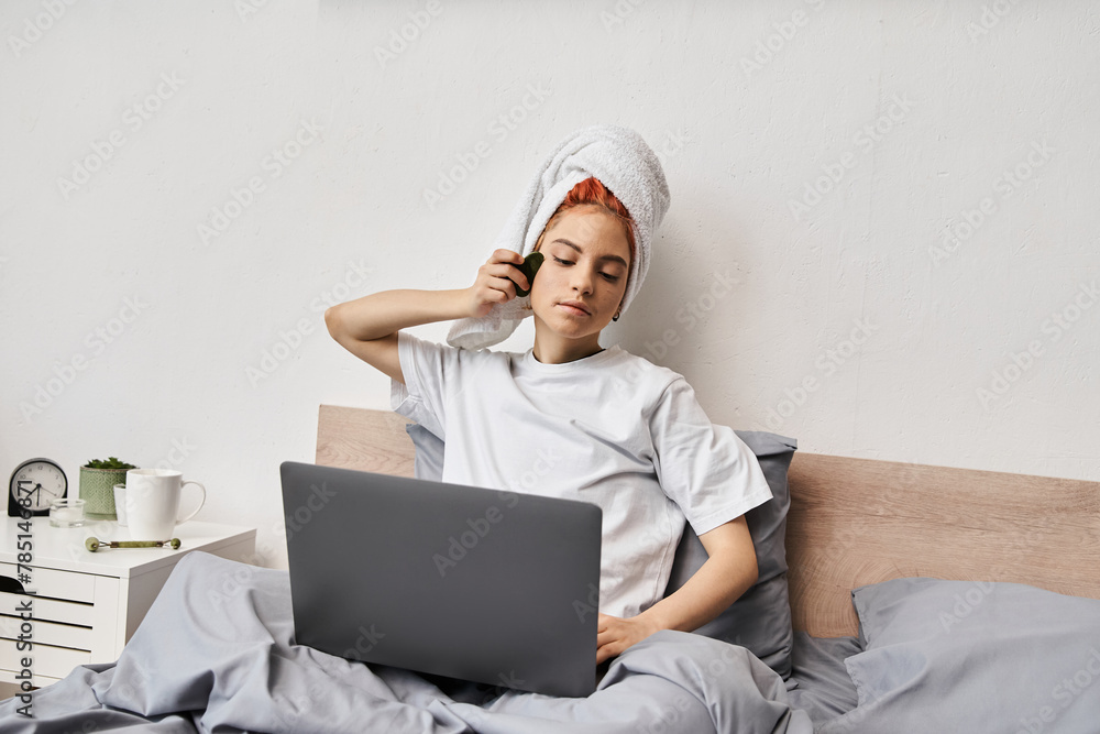 jolly pretty queer person with hair towel watching movies on laptop and using gua sha while in bed jolly pretty queer person with hair towel watching movies on laptop and using gua sha while in bed