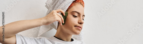 merry beautiful queer person with hair towel in homewear using gua sha while at home, banner photo