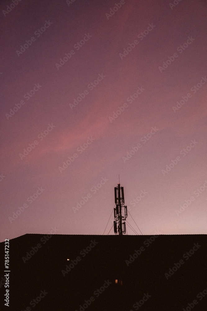 Naklejka premium Vertical shot of a base station on top of the apartment building against the magenta sunset sky