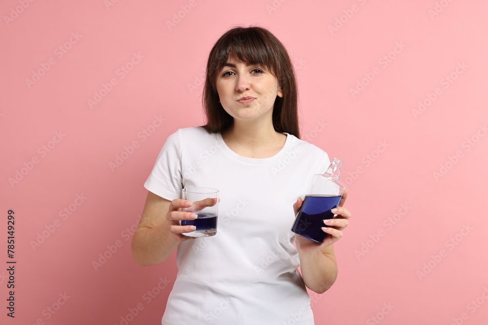 Young woman using mouthwash on pink background Young woman using mouthwash on pink background