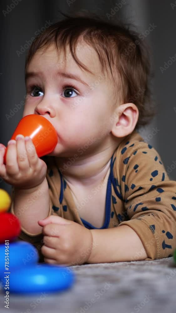 Cute toddler boy lying on the floor with toy pyramid. Lovely child took a toy top and put it into mouth. Blurred backdrop. Vertical video Cute toddler boy lying on the floor with toy pyramid. Lovely child took a toy top and put it into mouth. Blurred backdrop. Vertical video