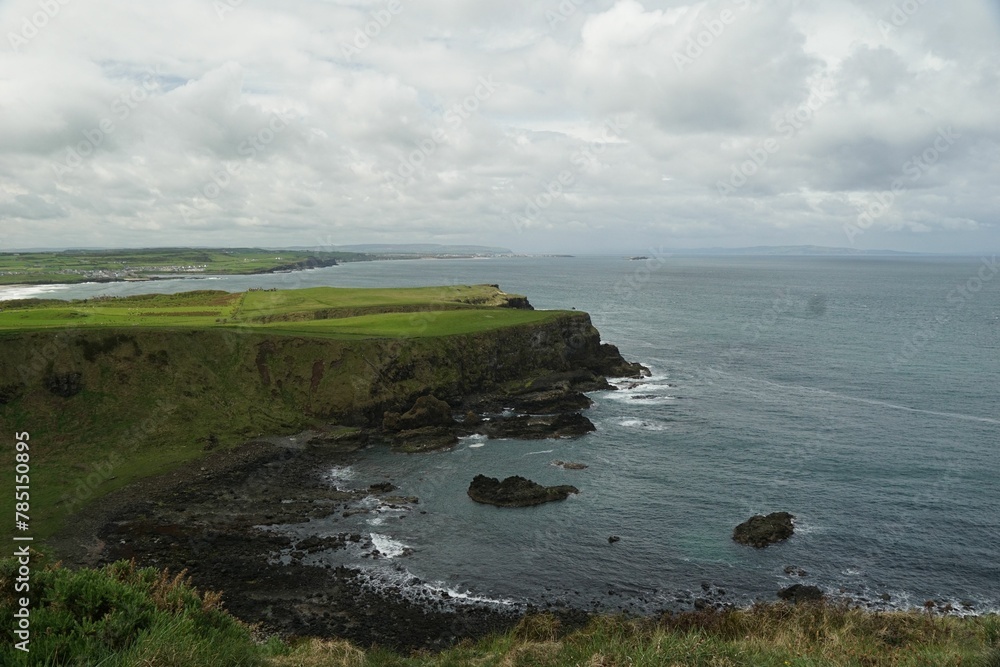 Scenic view of the sea with coastline cliffs covered with grass under the cloudy sky Scenic view of the sea with coastline cliffs covered with grass under the cloudy sky
