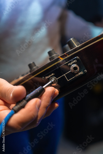 Close up man hand sticking plug to guitar in concert hall. Unrecognizable person connecting instrument in recording studio. Unknown sound engineer preparing electric guitar for playing.