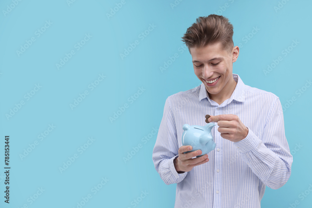 Happy man putting coins into piggy bank on light blue background. Space for text Happy man putting coins into piggy bank on light blue background. Space for text