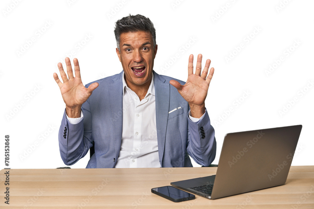 Elegant businessman at desk with laptop receiving a pleasant surprise, excited and raising hands. Elegant businessman at desk with laptop receiving a pleasant surprise, excited and raising hands.