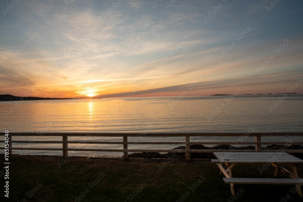 Wooden table and bench situated on a beach with a beautiful orange and pink sky in the background Wooden table and bench situated on a beach with a beautiful orange and pink sky in the background