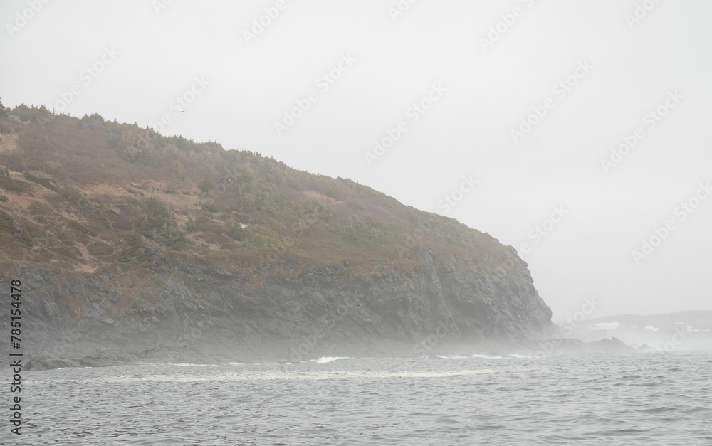 Scenic view of sea waves crashing against rocky cliffs on a stormy day in Newfoundland, Canada