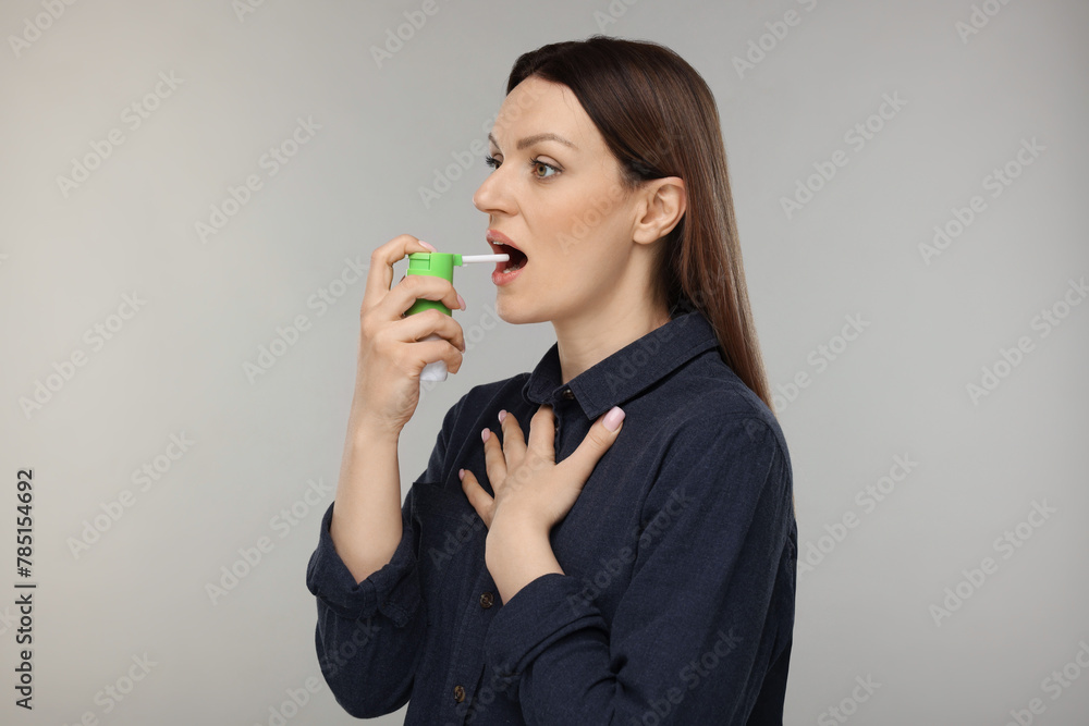 Woman using throat spray on grey background Woman using throat spray on grey background
