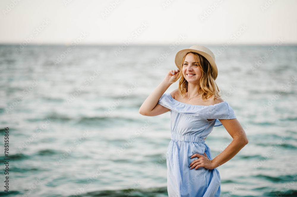 Young attractive smiling blond woman in straw hat joyfully walks near sea. Happy beautiful girl standing on beach ocean and enjoying sunny summer day on vacation. Portrait of stylish female closeup. Young attractive smiling blond woman in straw hat joyfully walks near sea. Happy beautiful girl standing on beach ocean and enjoying sunny summer day on vacation. Portrait of stylish female closeup.