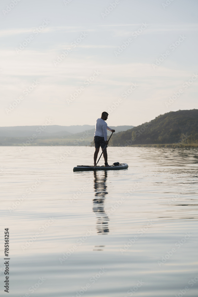 A man is standing and paddling on a paddleboard on the water. Enjoying the vacation.  Landscape in the background.