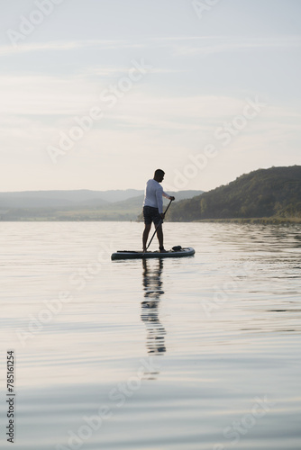 A man is standing and paddling on a paddleboard on the water. Enjoying the vacation. Landscape in the background.