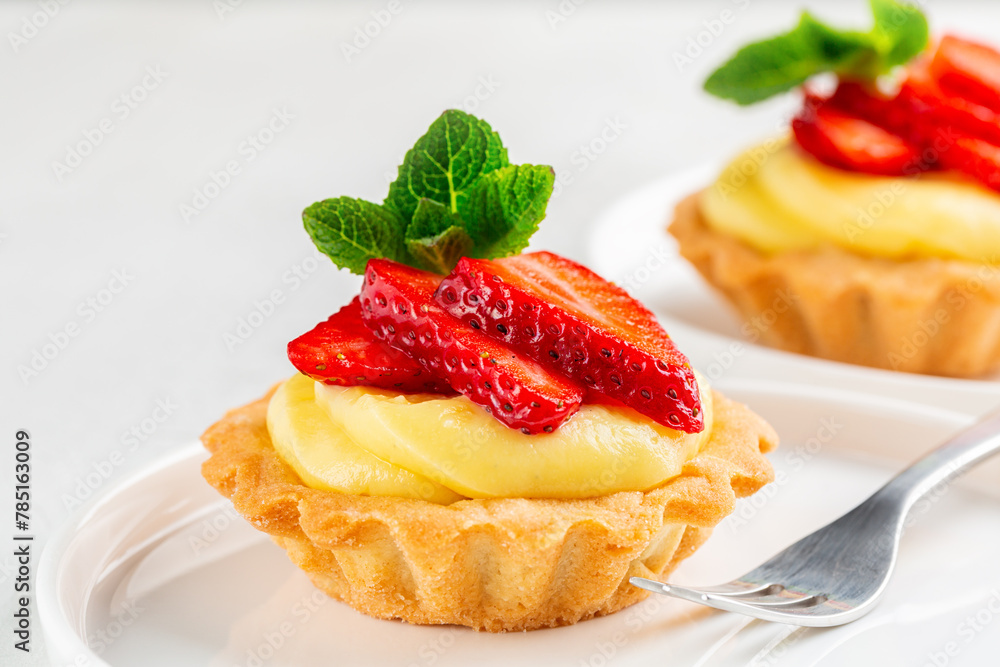 Close up of Strawberry tartlets with vanilla pastry cream - mini fruit tarts filled with custard vanilla pastry cream in a delicate cookie crust. Dessert. White background. Close up of Strawberry tartlets with vanilla pastry cream - mini fruit tarts filled with custard vanilla pastry cream in a delicate cookie crust. Dessert. White background.