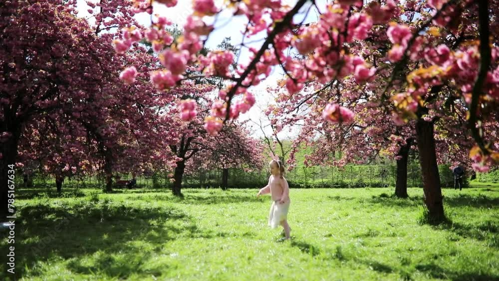 Adorable preschooler girl wearing bunny ears head decoration enjoying sunny spring day in Park of Sceaux near Paris, France. Beautiful child having fun under pink cherry blossom trees. Adorable preschooler girl wearing bunny ears head decoration enjoying sunny spring day in Park of Sceaux near Paris, France. Beautiful child having fun under pink cherry blossom trees.