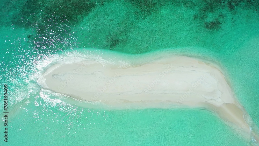 Aerial drone shot of a deserted tiny tropical island in the Maldives washed by the Indian Ocean