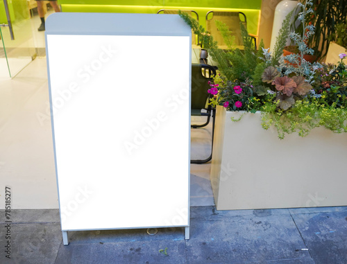 Blank white outdoor advertising stand or sandwich board mock up template. Clear street signage board placed by an outdoor dinning area of a restaurant. Background texture of standee on street. photo