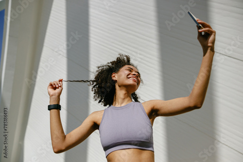 Portrait of sporty smiling young woman after running making selfie outdoors 
