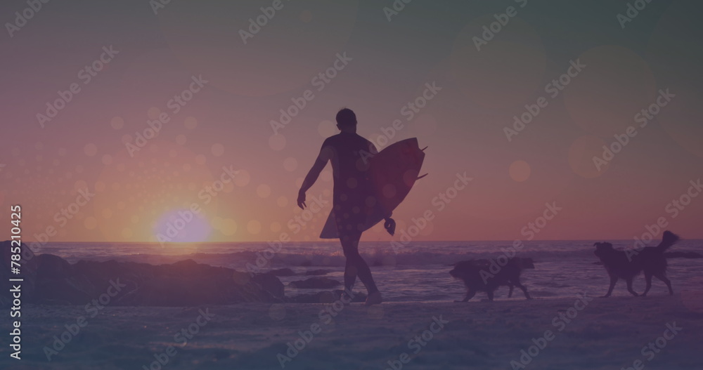 Image of glowing lights over man walking with surfboard by the sea