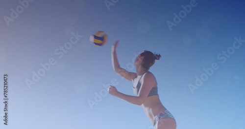 Image of glowing lights over caucasian woman playing beach volleyball by the sea © vectorfusionart