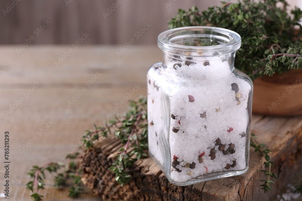 Salt with peppercorns in glass jar and thyme on wooden table, space for text Salt with peppercorns in glass jar and thyme on wooden table, space for text