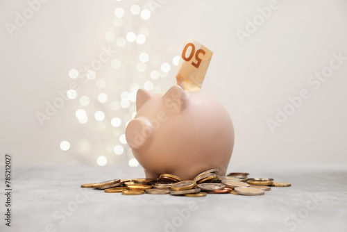 Piggy bank and coins on grey table against blurred lights