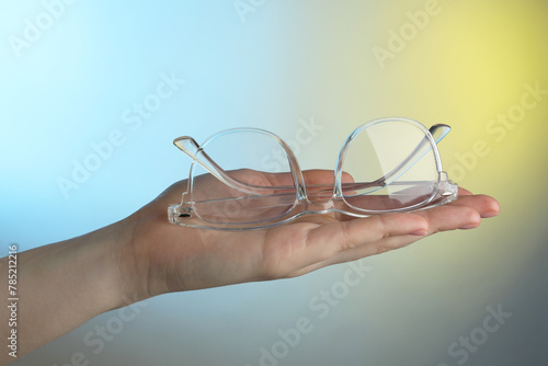 Woman holding glasses with transparent frame on color background, closeup