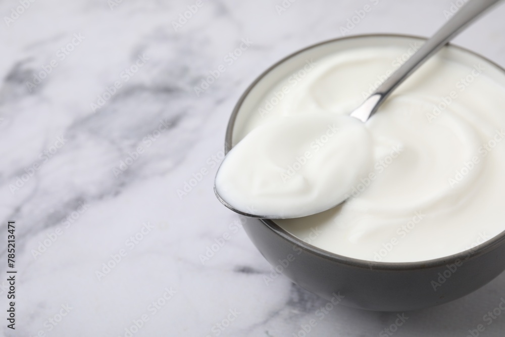 Delicious natural yogurt in bowl and spoon on white marble table, closeup. Space for text Delicious natural yogurt in bowl and spoon on white marble table, closeup. Space for text