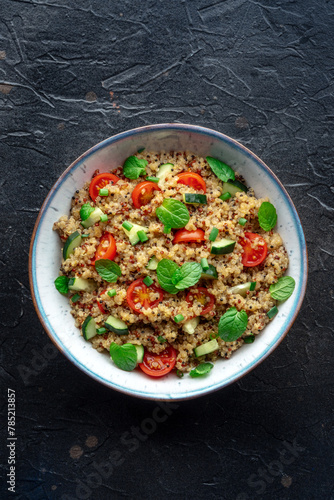 Quinoa tabbouleh salad in a bowl, a healthy dinner with tomatoes and mint, top shot on black
