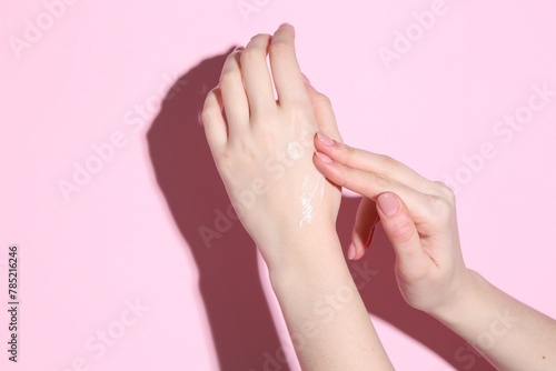 Woman applying cream on her hand against pink background, closeup