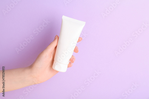 Woman with tube of cream on lilac background, closeup