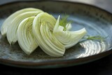 A finely sliced fennel bulb arranged on a contemporary plate, showcasing its crisp texture and mild licorice flavor.