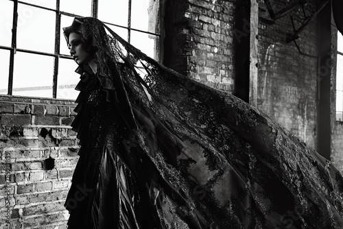 A gothcore fashion editorial showcasing a model draped in elaborate, dark lace and leather garments against an industrial backdrop. The juxtaposition of textures and the bold, monochromatic styling