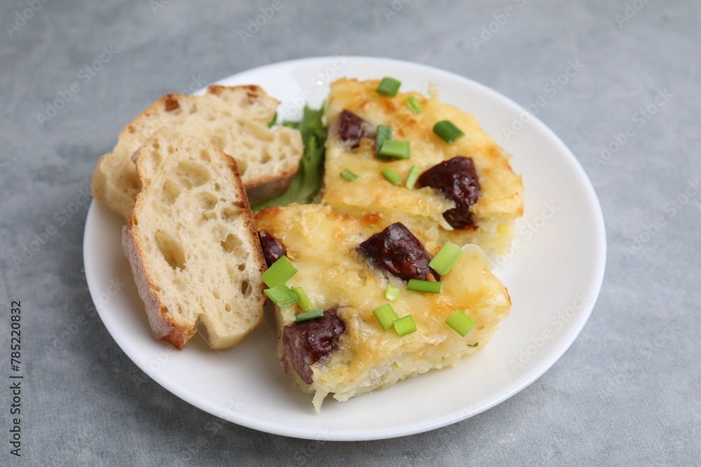 Tasty sausage casserole with green onion and bread on grey table, closeup