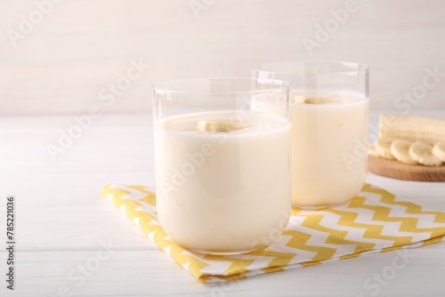 Tasty yogurt and banana in glasses on white wooden table, closeup. Space for text