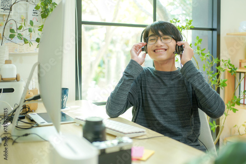 Happy relaxed teenager man.  Asian student boy rest and use headphone listening music broadcast feel and game after using laptop for distance education and doing homework online.